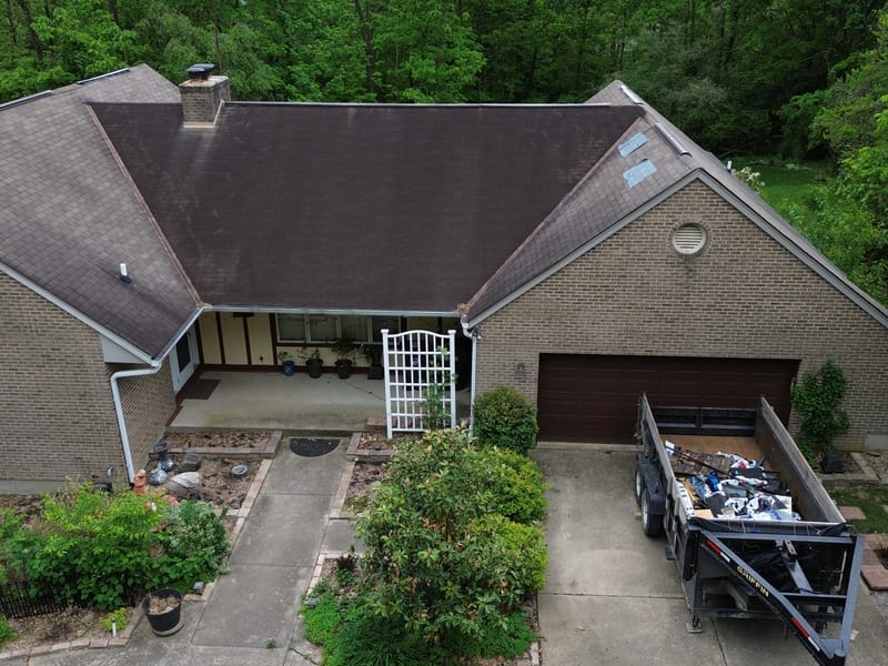 Drone view at eave height of the brick ranch before work, its old dark three-tab roof weathered and streaked