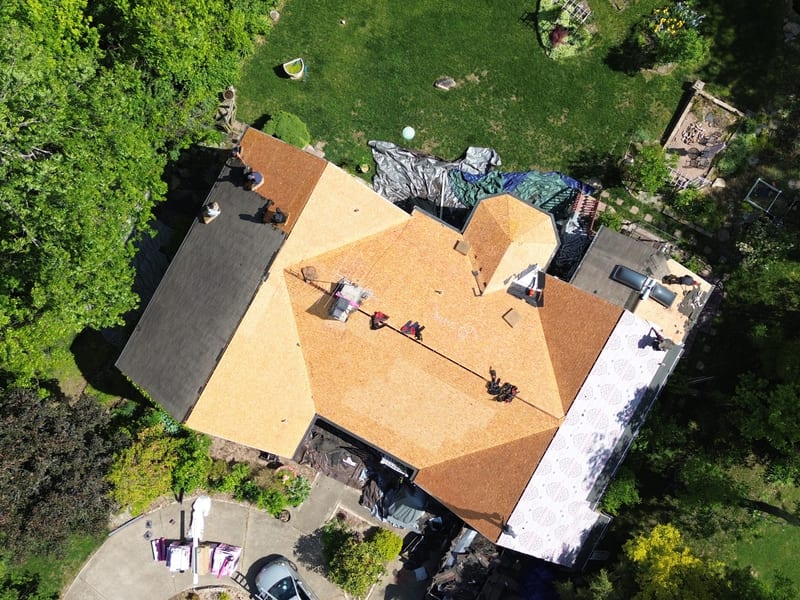 Aerial of the roof stripped clean to bare decking with shingle bundles staged on the driveway below