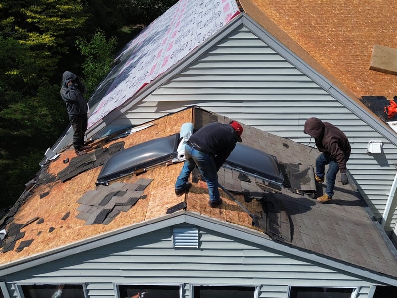 Two roofers stripping shingles around the pair of skylights with the decking opened up beside them