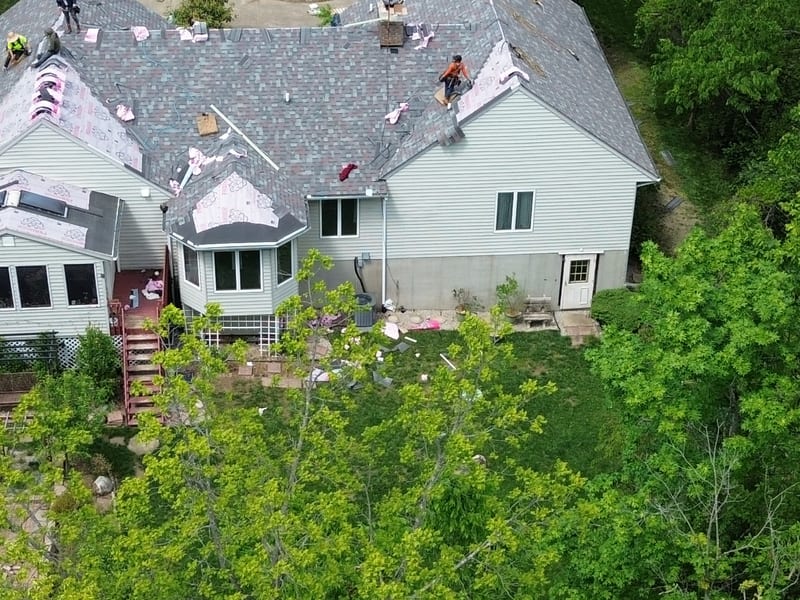 Wide view of the rear elevation on its wooded hillside with the new roof on, walkout level and deck below