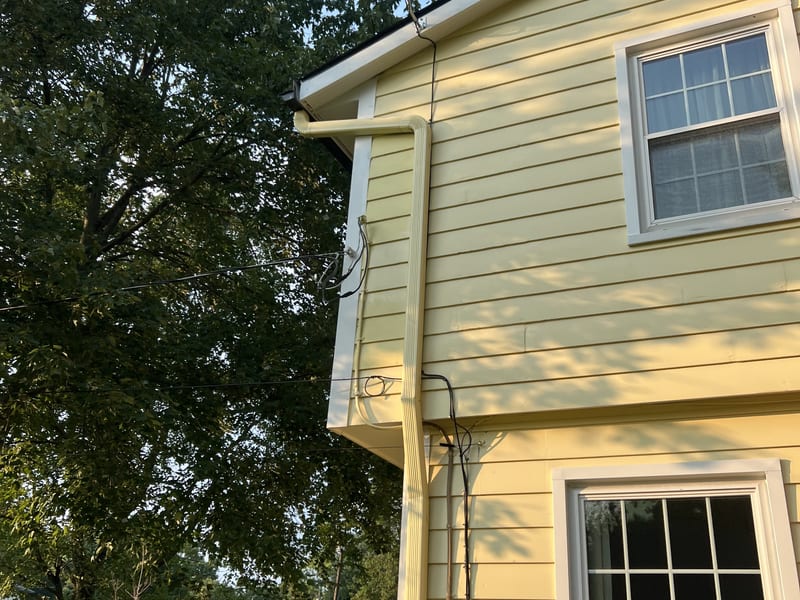 Golden-hour view of the two-story yellow lap-siding elevation with the repaired corner and the downspout strapped full height