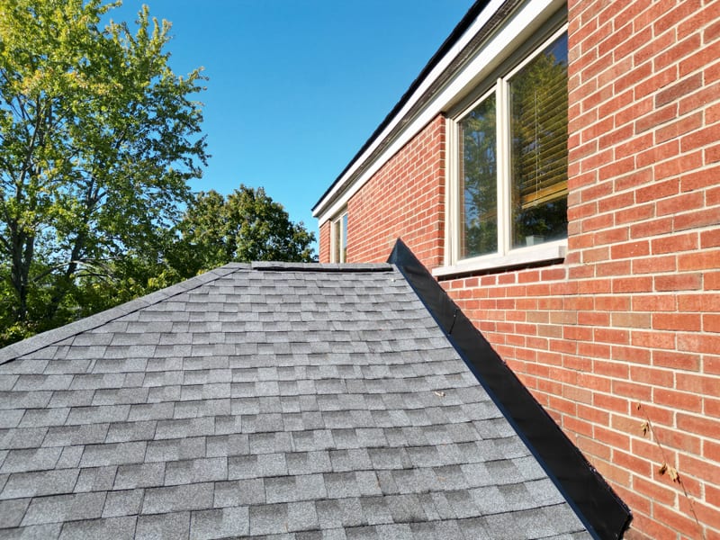 Low-angle view of a finished lower roof section against the brick wall with new step and counter flashing