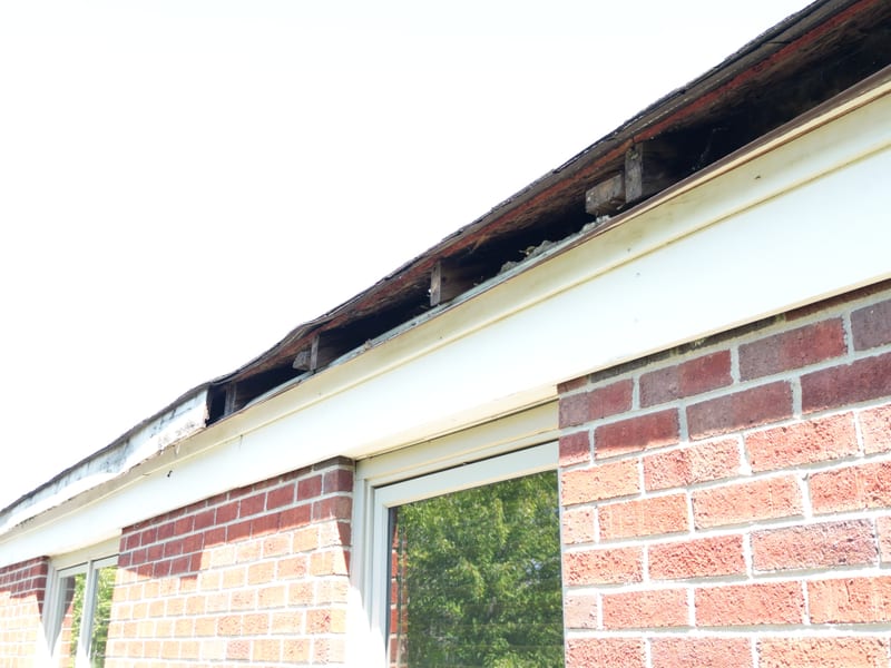 Low-angle eave detail before the work showing deteriorated decking behind the gutter line