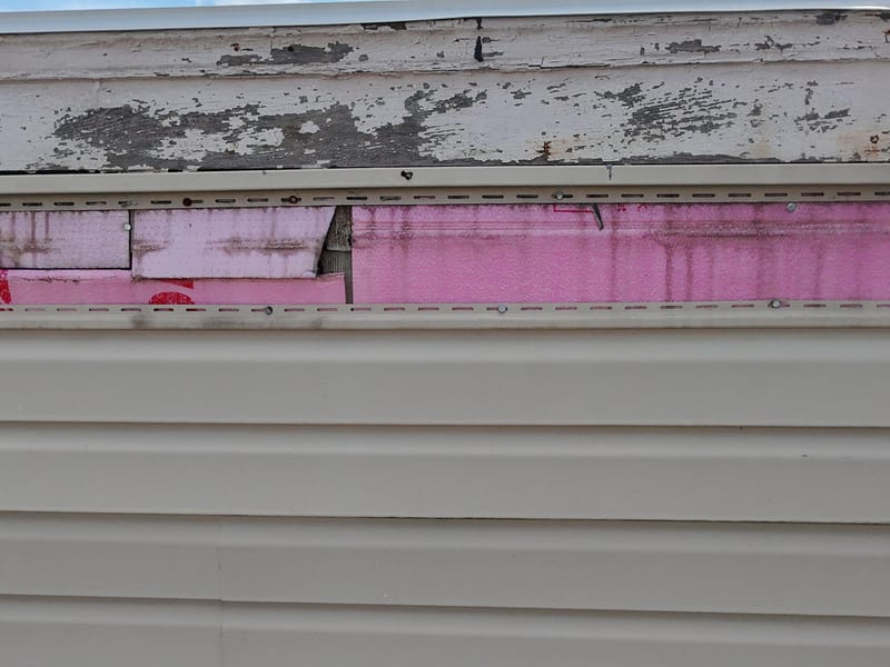 The top course of vinyl siding missing along the run at the head of a two-story wall, leaving the cavity open