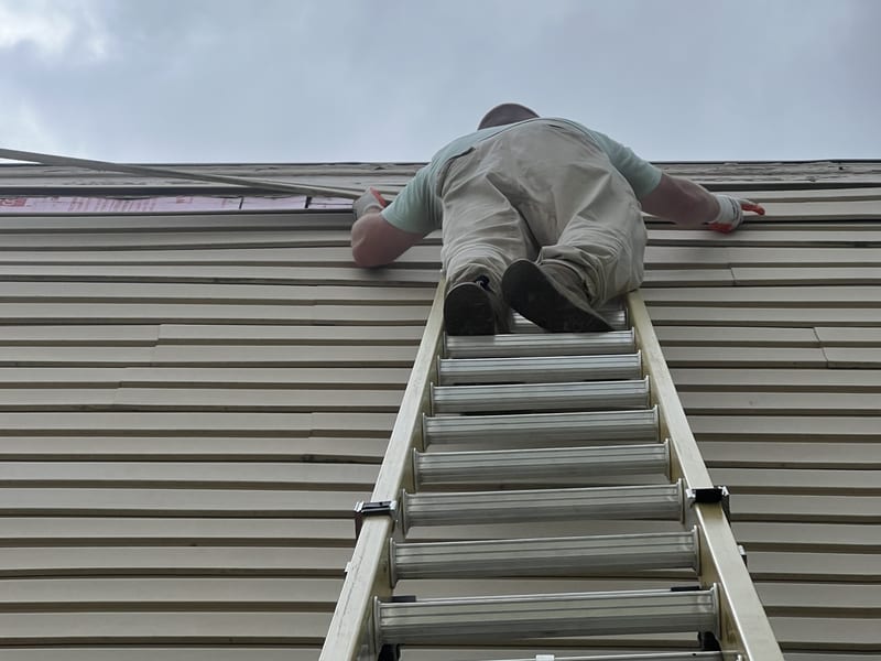 Looking up the extension ladder at the open course with the worker seen from behind