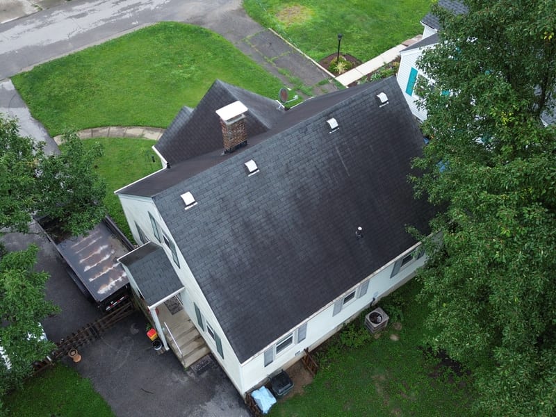 Angled aerial down the long slope showing how steep the 10/12 pitch is, with the valley, chimney and dormer gable in frame