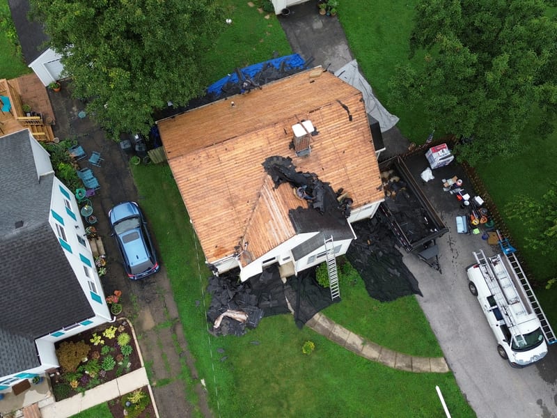 Top-down view after tear-off with the roof stripped to bare plank sheathing and old shingles piled on tarps below