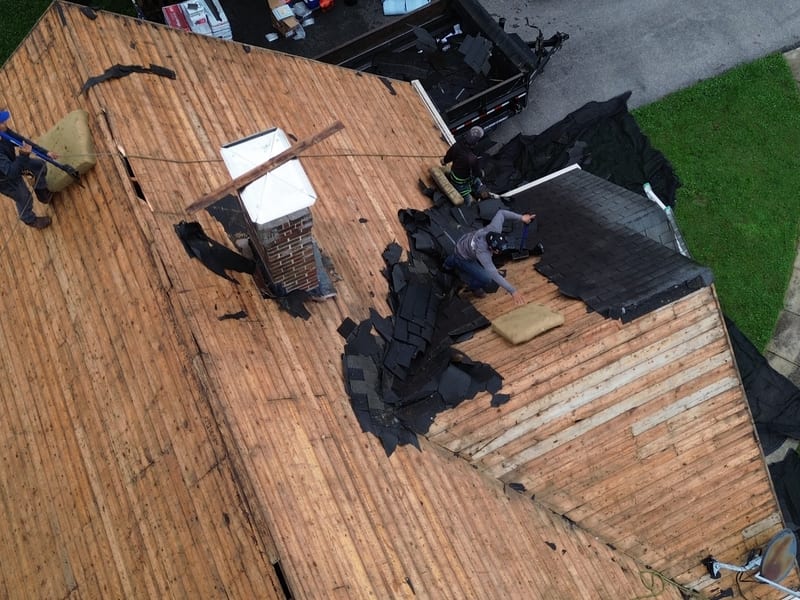 Three crew working the stripped deck around the masonry chimney ahead of the re-flash