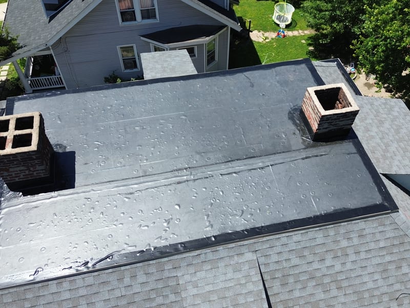 Straight-down view of the finished third-story flat roof with the new membrane fully adhered and both chimneys re-flashed