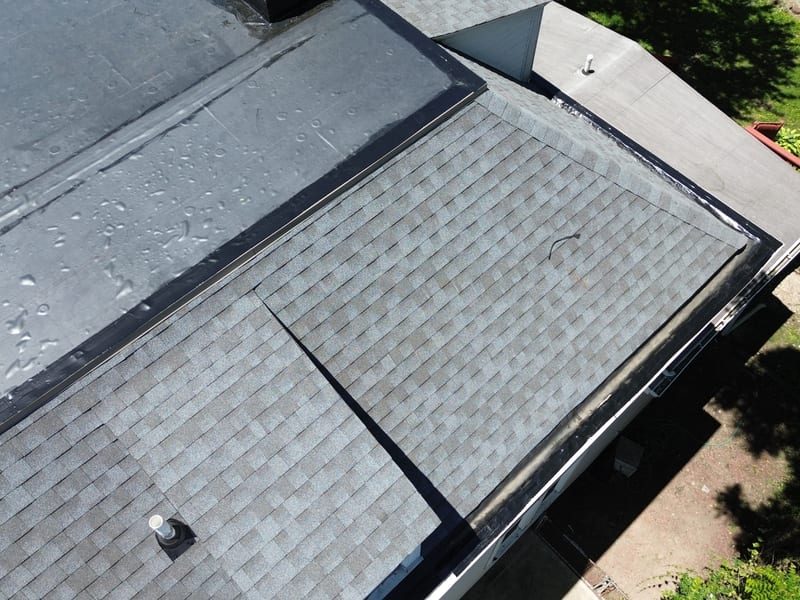 Close view of the transition itself: new membrane on one side, new pewter-grey shingle on the other, joined with fresh edge metal