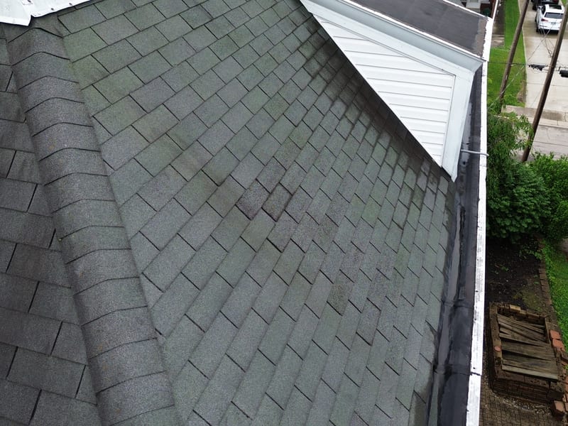 Close view of the steep mansard with granule-worn three-tab shingles and a mismatched patch repair mid-field
