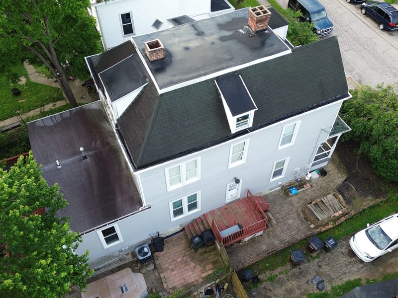 Aerial over the rear of the three-story house before the work, aged dark-green shingles on the mansard and the failing flat above