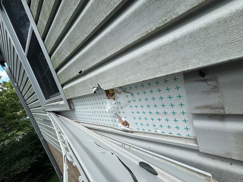 The wind damage up close: torn siding, punctured foam sheathing, and a bent gutter above the porch roof