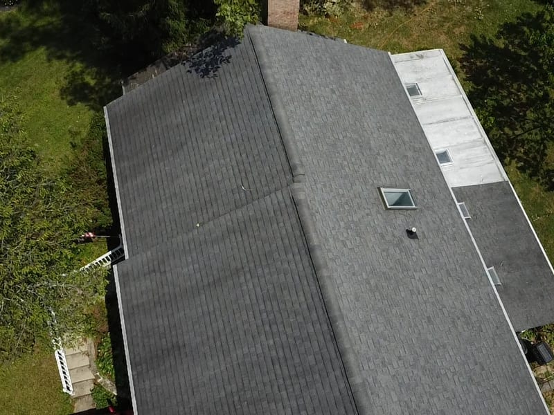 Overhead drone view of the home's gray shingle roof and white flat-roof section on inspection day