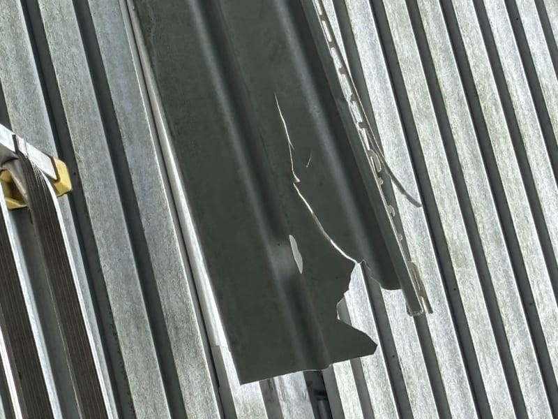 Storm-torn vinyl siding panel ripped open and hanging off the wall