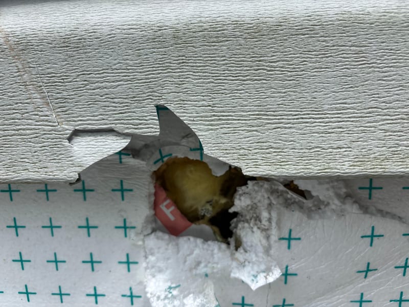 Impact hole punched clean through the siding and foam sheathing with insulation showing