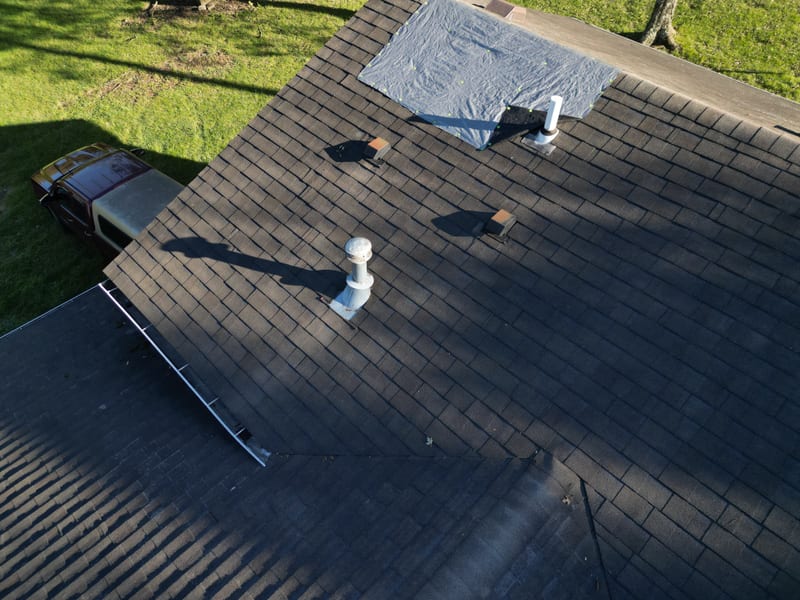 The same wind-damaged roof with an emergency tarp cap-nailed over the exposed ridge